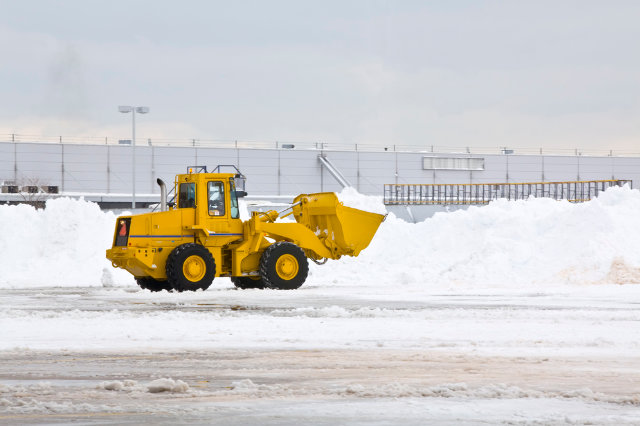 Yellow snow truck moving snow in a parking lot.