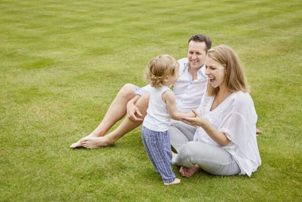 Couple with baby sitting happily on a green lawn.